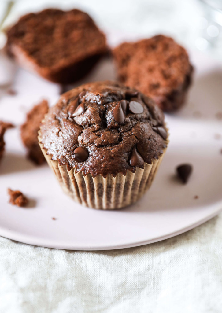 A straight on view of a chocolate muffin on a pink plate. 