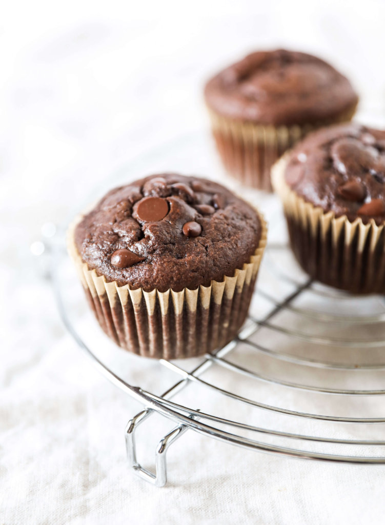 A straight on view of a chocolate muffin on a circular cooling rack with other muffins in the background. 